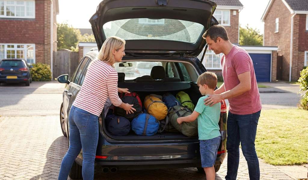 Family packing suitcases and bags into a car trunk